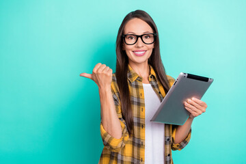 Photo of impressed mature brunette lady indicate empty space hold tablet wear eyewear yellow shirt isolated on teal color background