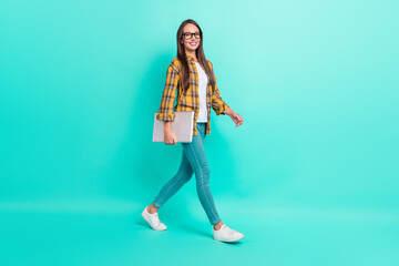 Fototapeta na wymiar Full length profile photo of hr young brunette lady go hold laptop wear eyewear shirt jeans shoes isolated on teal background