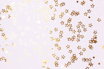 Metallic gold colored glittering stars confetti scattered on a white background.