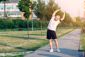In the morning at sunrise, a man with an interesting braid hairstyle in headphones stretches before jogging