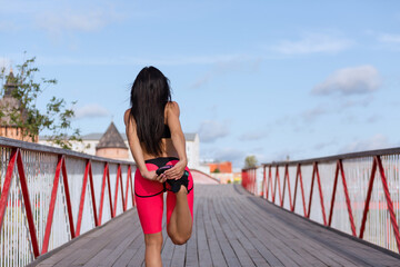 A woman in a pink sweat suit stretches on a bridge before jogging