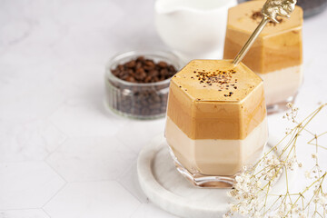 Two glasses with trendy korean beverage dalgona coffee latte - whipped instant coffee, sugar and hot water and milk layers on a marble board, white surface