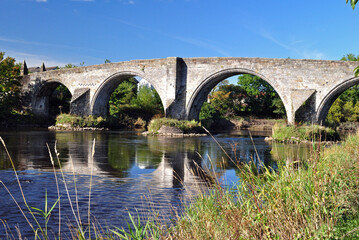 View of Ancient Stone Bridge & River with Grassy River Bank  against Blue Sky 