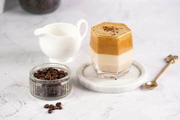 glass with trendy korean beverage dalgona coffee latte - whipped instant coffee, sugar and hot water and milk layers on a marble board, white surface