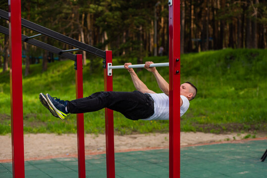 Caucasian man doing a back plank on the uneven bars. Workout on the sports ground.