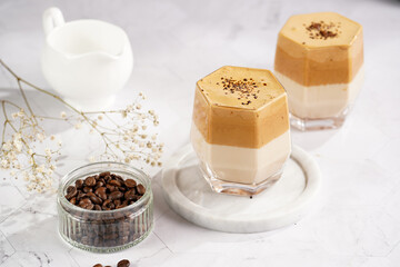 Two glasses with trendy korean beverage dalgona coffee latte - whipped instant coffee, sugar and hot water and milk layers on a marble board, white surface
