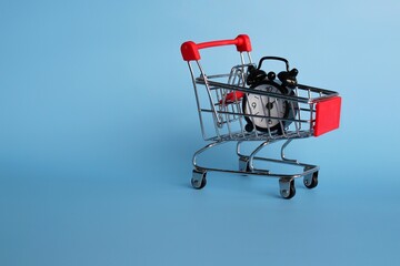 Business and finance concept. Alarm clock and shopping trolley on blue background. Copy space for text.