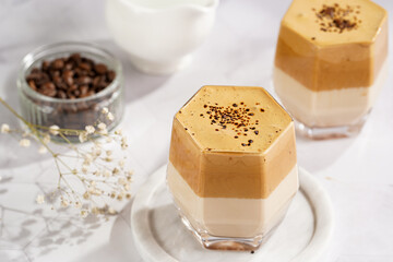 Two glasses with trendy korean beverage dalgona coffee latte - whipped instant coffee, sugar and hot water and milk layers on a marble board, white surface