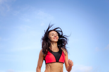Naklejka premium Attractive brunette woman in red sportswear runs against the blue sky