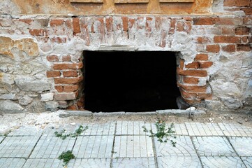secret lair in an abandoned building with a dark hole that acts as a window at ground level, in a textured brick wall