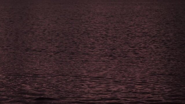 Close-up of the gentle ripples of the calm sea at dusk, the water presents a reddish color with infinite small shadows.