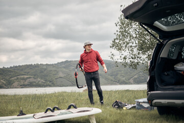 Windsurfer and camper packing and unpacking from a car in nature.