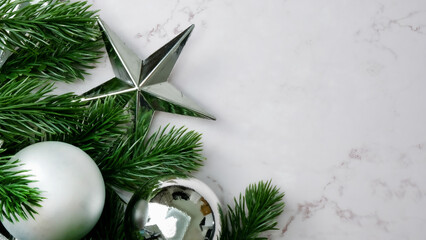 Green pine tree leaves on white marble background, christmas decorations in bright silver color. Simple and creative christmas concept.