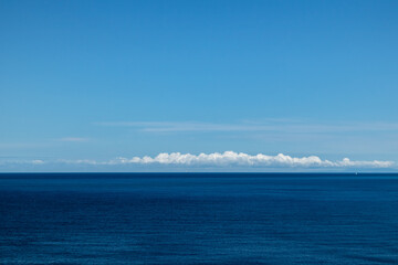 Fototapeta premium Blue Ionian sea landscape and skyscape view in Greece. Bright day with low scenic white clouds over dark deep blue water surface