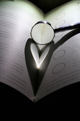 Lupa sobre el libro con luz lateral forma un diseño de corazòn con luces y sombra sobre la hoja...