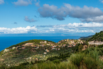 Picturesque traditional greek village with tiled roofs on hills full of greenery near blue sea shore on Lefkada island, Greece. Travel Europe in summer