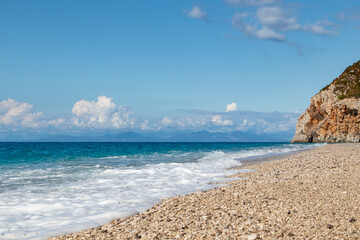 Mylos sandy beach with azure sea, stormy waves, white foam and rocky cliff on coast of Lefkada island in Greece. Summer nature vacation travel to Ionian Sea
