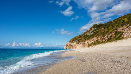 Mylos beach with azure stormy waves with white foam and green rocky cliffs on coast of idyllic Lefkada island in Greece. Summer vacation, travel to vibrant scenic Ionian Sea