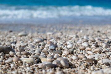White wet pebble stones close-up on beach with blue tide waves. Coast of Lefkada island in Greece. Summer nature of Ionian Sea