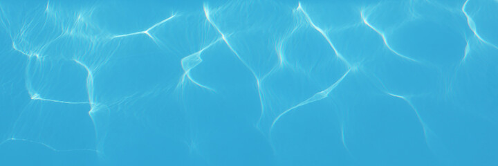 Water background. Blue swimming pool pattern with natural rippled water texture. Top view with copy space. Panoramic banner
