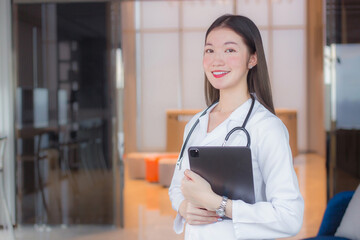 Young Asian professional woman doctor in white lab coat holds tablet in her hand at the clinic in the hospital.