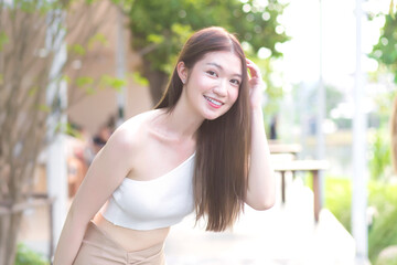Young Asian beautiful woman with good skin in cream shirt standing smiling happily on blurred background.