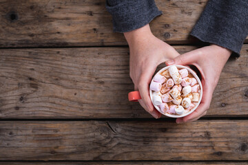 Female hands holding mug of hot chocolate drink filled with marshmallows at table with copy space