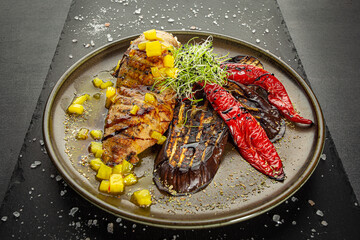 Grilled chicken breast with pineapple and grilled vegetables. A dish of author's cuisine on a dark background.