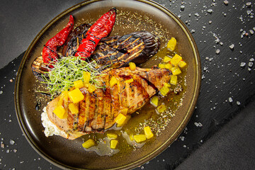 Grilled chicken breast with pineapple and grilled vegetables. A dish of author's cuisine on a dark background.
