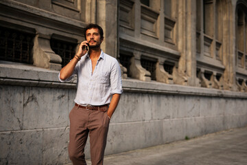 Obraz premium Young stylish man using the phone outdoors. Fashion happy man talking to the phone.