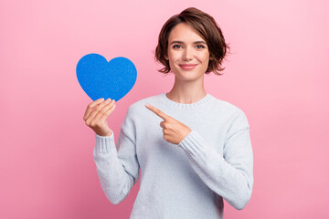 Photo of cheerful nice young woman hold blue heart paper shape point finger isolated on pink color...