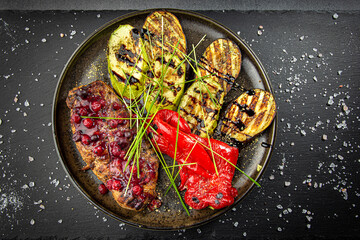 Baked pork meat glazed with cranberry sauce and grilled vegetables, served with green sprouts