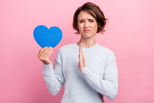Photo of unhappy upset sad young woman hold blue heart paper shape hand refuse isolated on pink color background