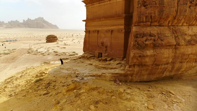 Aerial Reversing From A Woman Standing In Front Of An Ancient Tomb Carved Into The Side Of A Desert Rock Formation - Arabian Desert, Saudi Arabia