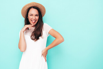 Young beautiful smiling female in trendy summer clothes. Sexy carefree woman posing near blue wall in studio. Positive brunette model having fun. Cheerful and happy. Shows tongue