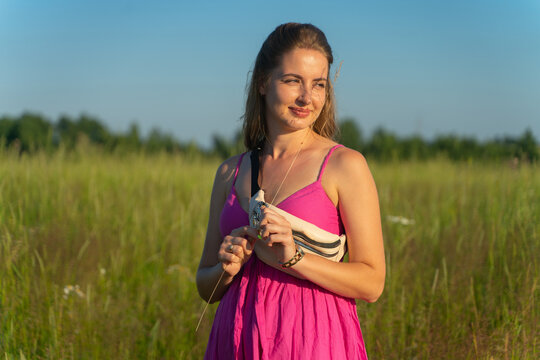 A girl in a pink dress stands in the field