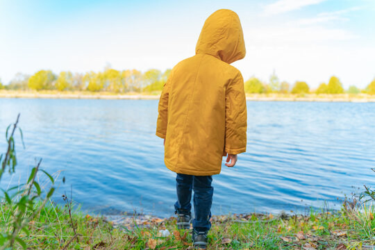 A boy in a yellow jacket stands near the lake