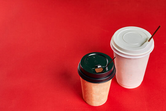 Two single-use plastic coffee cups on red background with copy space