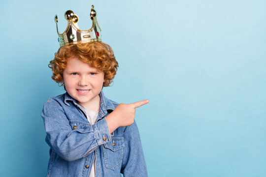 Photo portrait curly little boy smiling pointing finger copyspace wearing crown isolated pastel blue color background