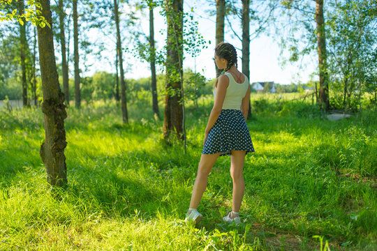 A girl in a skirt and T-shirt walks through the woods
