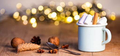 christmas banner with cup with hot chocolate and marshmallows on with cinnamon sticks and fir xmas tree branches with beautiful bokeh lights. New year celebration