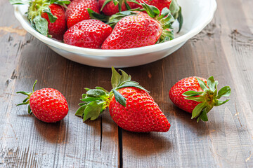 fragrant ripe strawberries in a white bowl on a wooden surface