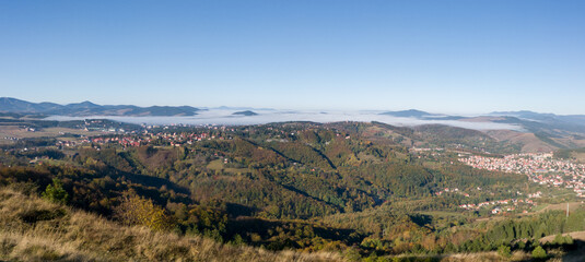 Naklejka premium Panoramic view of the forested Zlatibor mountain and parts of the tourist towns of Zlatibor and Cajetina and the nearby peaks that break through the fog in October