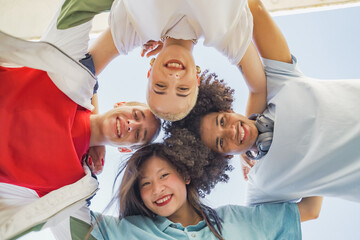 Low angle view of multiethnic young trendy friends hugging, smiling and making a circle with their heads.