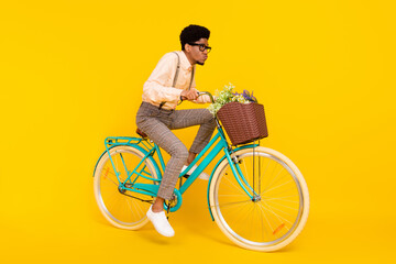 Full length body size photo man riding bike with flowers basket in glasses isolated vivid yellow...