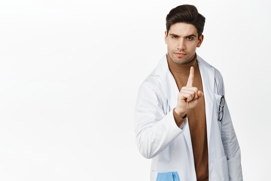 Image Of Doctor Saying No, Scolding, Shaking Finger In Disapproval And Looking Skeptical At Camera, Standing Over White Background