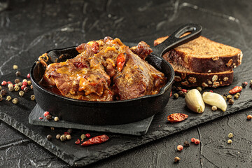Pork stew in frying pan on black background, close up view