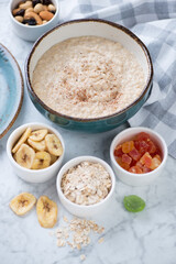 Bowl of oatmeal porridge with various toppings over light-grey marble background, vertical shot
