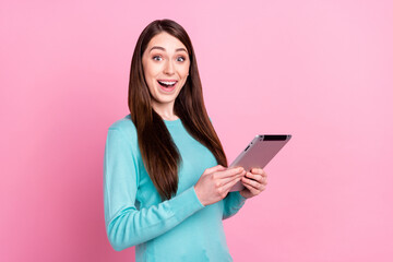 Photo of positive amazed young woman hold hands tablet network shocked isolated on pink color background