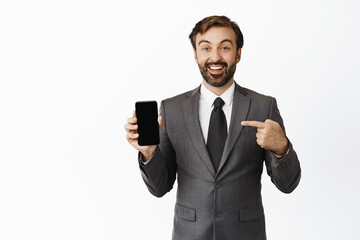 Excited smiling business man pointing finger at mobile phone screen, showing chart, company website on smartphone, white background